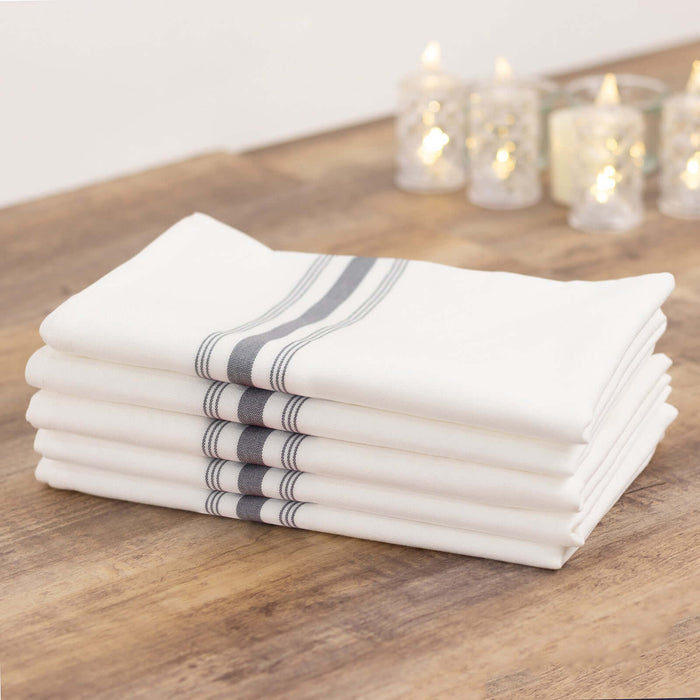 Stack of white kitchen towels with gray stripes on a wooden table.