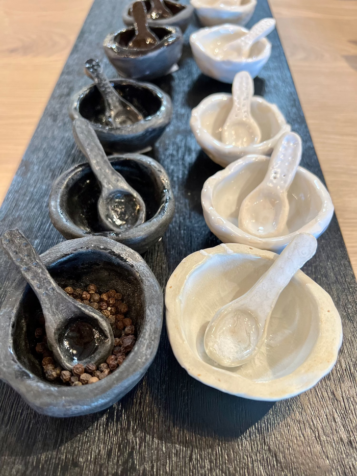 Handmade salt and pepper set: multiple speckled ceramic bowls with spoon handles, arranged in pairs