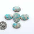 Carico Lake Turquoise cabochons, aqua-blue to turquoise gemstones with natural matrix on a white background with a US dime for scale