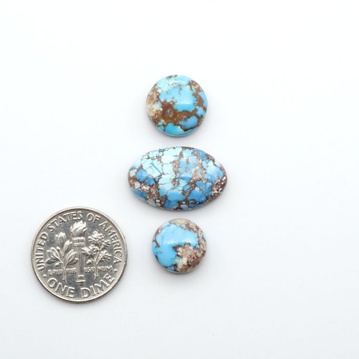 Golden Hills Turquoise cabochons, icy blue to lavender tones with chocolate matrix, polished stones on a white background with a US dime for scale