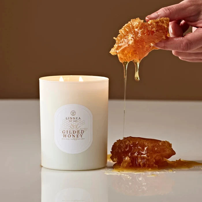 Lit white candle with twin wicks; golden honey wax drip in hand