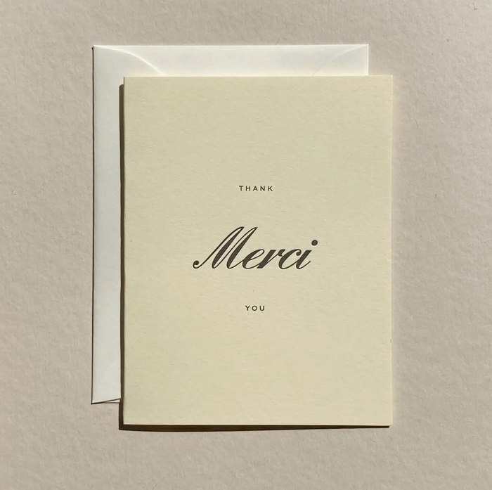 Cream Merci greeting card with black text: THANK YOU and cursive Merci