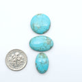 Pilot Mountain Turquoise cabochons, blue-green gemstones with natural matrix on a white background with a US dime for scale
