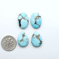 Pressed Turquoise nugget cabochons, stabilized composite with blue color and dark matrix on a white background, with a US dime for size