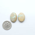 Two oval stones with turquoise stripes next to a U.S. dime on a white background. Royston Turquoise cabochons are famous for their distinctive matrix and unique green and blue hues, making them a favored option among jewelry designers.