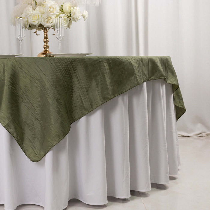 Olive green tablecloth draping over white table with floral centerpiece.
