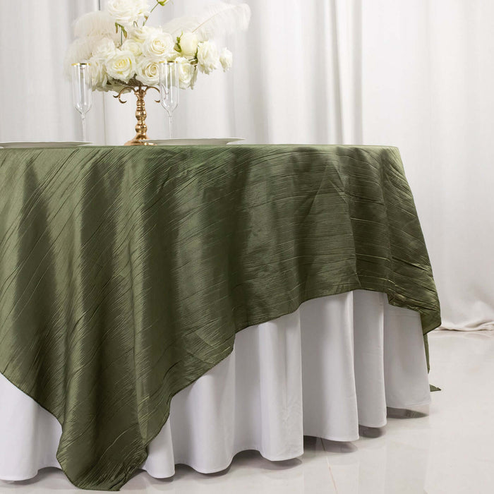 Olive green tablecloth draped over a white table with floral centerpiece.